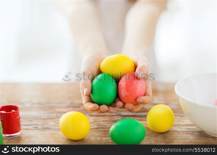 easter, holiday and child concept - close up of little girl holding colored eggs with colors and bowl on the table