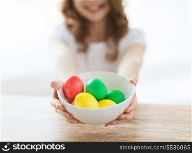 easter, holiday and child concept - close up of little girl holding bowl with colored eggs