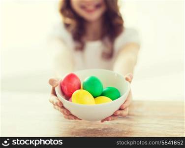 easter, holiday and child concept - close up of little girl holding bowl with colored eggs