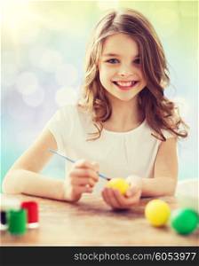 easter, holiday and child concept - happy girl with brush coloring easter eggs over lights background