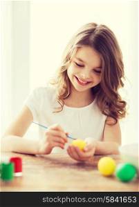 easter, holiday and child concept - smiling little girl coloring eggs for easter
