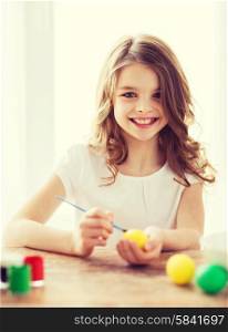 easter, holiday and child concept - smiling little girl coloring eggs for easter