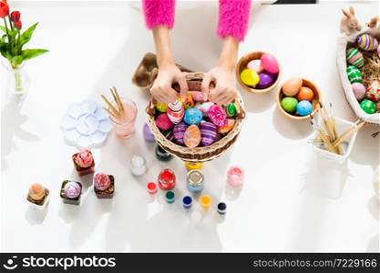 Easter holiday concept, Close up of hand of holding wearing bunny ears hand holding a basket with colorful Easter eggs on white wooden table background in top view