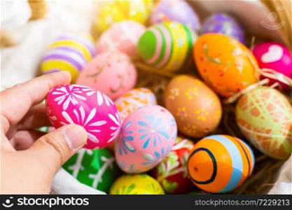 Easter holiday concept, Close up of man holding a colorful Easter egg in egg box,basket Easter eggs on white pastel color rustic wood background with space.