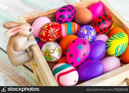 Easter holiday concept,Garden ornaments rabbit statues with Colorful Easter eggs in basket on white pastel color rustic wood background with space.
