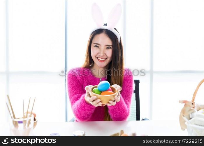 Easter holiday concept, Happy Asian Young woman hand show holding a basket with colorful Easter eggs In the white room background