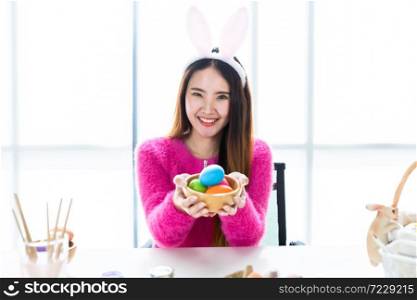 Easter holiday concept, Happy Asian Young woman hand show holding a basket with colorful Easter eggs In the white room background