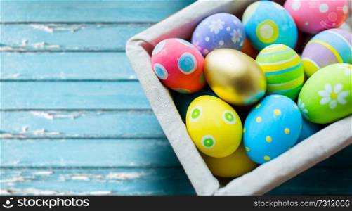 easter, holidays and object concept - close up of colored eggs in basket over blue vintage wooden boards background. close up of colored easter eggs in basket