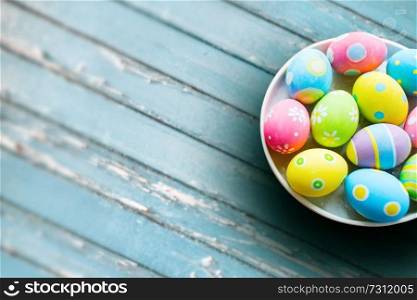 easter, holidays and object concept - close up of colored eggs on plate over blue vintage wooden boards background. close up of colored easter eggs on plate