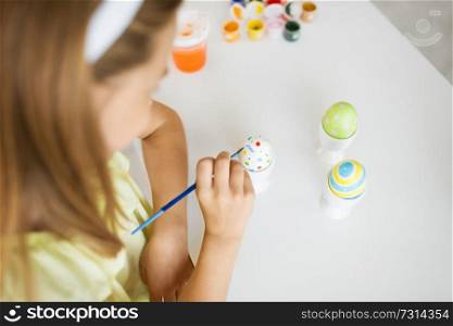 easter, holidays and people concept - close up of girl coloring egg by paintbrush. close up of girl coloring easter egg by paintbrush