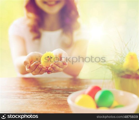 easter, holidays and people concept - close up of girl holding yellow chicken toy and colored eggs on table