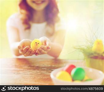 easter, holidays and people concept - close up of girl holding yellow chicken toy and colored eggs on table
