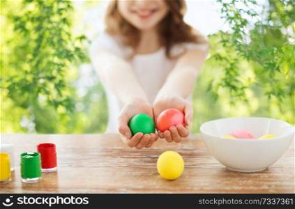 easter, holidays and people concept - close up of girl&rsquo;s hands holding colored eggs over green natural background. close up of girl holding colored easter eggs
