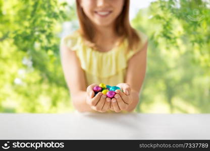 easter, holidays and people concept - close up of happy girl holding chocolate eggs in colorful foil wrappers over green natural background. close up of girl holding chocolate easter eggs