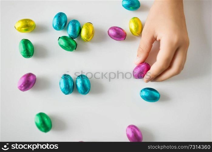 easter, holidays and people concept - hand of child with chocolate eggs or candies in foil wrappers. hand of child with chocolate easter eggs in foil