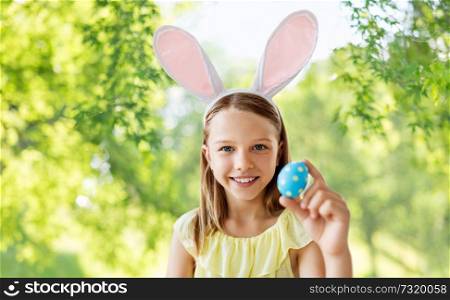 easter, holidays and people concept - happy girl wearing bunny ears headband with colored egg over green natural background. happy girl with colored easter egg