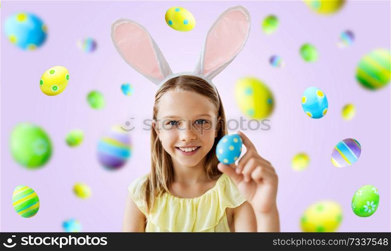 easter, holidays and people concept - happy girl wearing bunny ears headband with colored egg over violet background. happy girl with colored easter egg over violet
