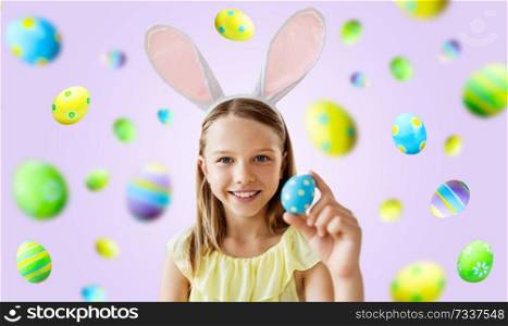 easter, holidays and people concept - happy girl wearing bunny ears headband with colored egg over violet background. happy girl with colored easter egg over violet