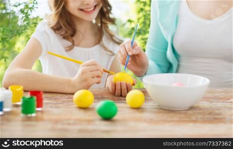 easter, holidays and people concept - happy smiling girl with mother coloring eggs over green natural background. happy smiling girl and mother coloring easter eggs