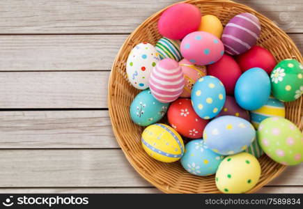 easter, holidays and tradition concept - close up of colored eggs in wicker basket on grey wooden boards background. close up of colored easter eggs in basket