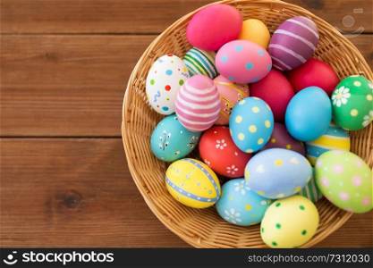 easter, holidays and tradition concept - close up of colored eggs in basket on wooden table. close up of colored easter eggs in basket