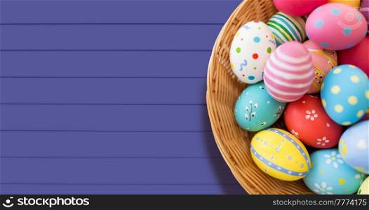 easter, holidays and tradition concept - close up of colored eggs in basket over violet background. close up of colored easter eggs in basket