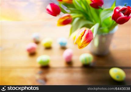 easter, holidays and tradition concept - close up of tulip flowers and colored eggs on wooden table. close up of tulip flowers and easter eggs
