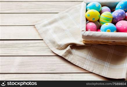 easter, holidays and traditions concept - close up of colored eggs in basket over grey wooden boards background. close up of colored easter eggs in basket
