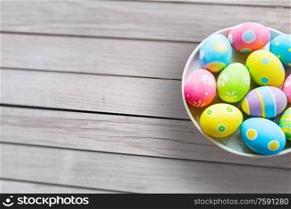 easter, holidays and traditions concept - close up of colored eggs on plate over grey wooden boards background. close up of colored easter eggs on plate