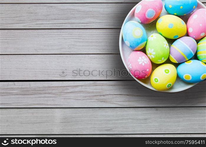 easter, holidays and traditions concept - close up of colored eggs on plate over grey wooden boards background. close up of colored easter eggs on plate