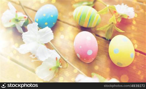 easter, holidays, spring, tradition and object concept - close up of colored easter eggs and flowers on wooden surface. close up of colored easter eggs and flowers