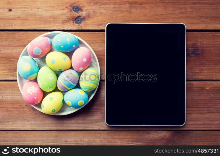 easter, holidays, technology, advertisement and object concept - close up of colored easter eggs on plate and blank tablet pc computer