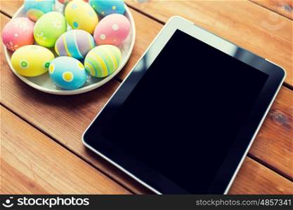 easter, holidays, technology, advertisement and object concept - close up of colored easter eggs on plate and blank tablet pc computer