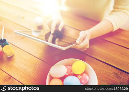 easter, holidays, technology and people concept - close up of woman hands with tablet pc computer, easter eggs and colors