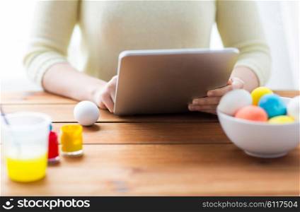 easter, holidays, technology and people concept - close up of woman hands with tablet pc computer, easter eggs and colors