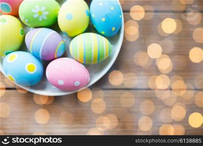 easter, holidays, tradition, advertisement and object concept - close up of colored easter eggs on plate over holidays lights
