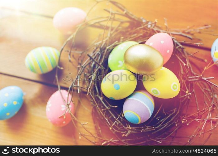 easter, holidays, tradition and object concept - close up of colored easter eggs in nest on wooden surface