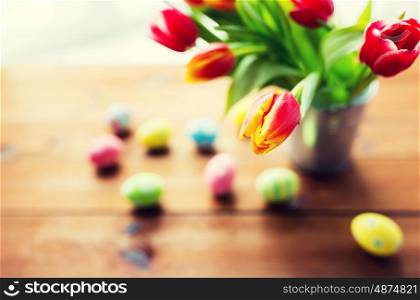 easter, holidays, tradition and object concept - close up of colored easter eggs and tulip flowers in bucket on wooden table