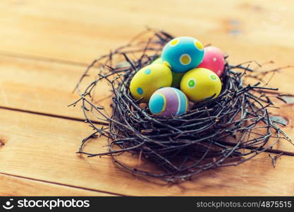 easter, holidays, tradition and object concept - close up of colored easter eggs in nest on wooden surface