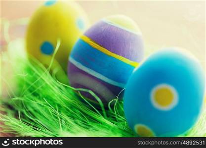easter, holidays, tradition and object concept - close up of colored easter eggs and decorative grass on wooden surface