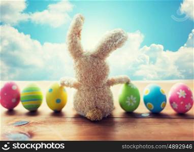 easter, holidays, tradition and object concept - close up of colored easter eggs and bunny over blue sky and clouds background
