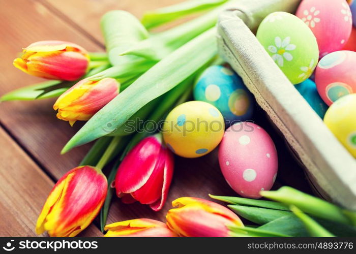 easter, holidays, tradition and object concept - close up of colored easter eggs in basket and tulip flowers