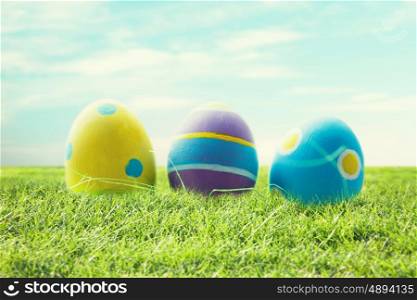 easter, holidays, tradition and object concept - close up of colored easter eggs and decorative grass on wooden surface over blue sky and grass background