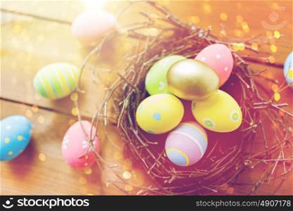 easter, holidays, tradition and object concept - close up of colored easter eggs in nest on wooden surface. close up of colored easter eggs in nest on wood