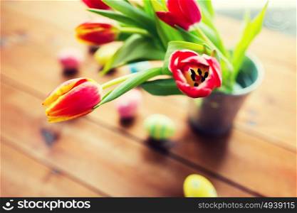 easter, holidays, tradition and object concept - close up of colored easter eggs and tulip flowers in bucket on wooden table. close up of easter eggs and flowers in bucket