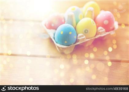 easter, holidays, tradition and object concept - close up of colored easter eggs in egg box or carton wooden surface. close up of colored easter eggs in egg box
