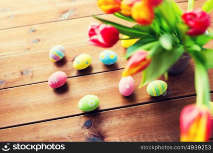 easter, holidays, tradition and object concept - close up of colored easter eggs and tulip flowers in bucket on wooden table. close up of easter eggs and flowers in bucket
