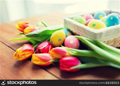 easter, holidays, tradition and object concept - close up of colored easter eggs in basket and tulip flowers. close up of colored easter eggs and flowers