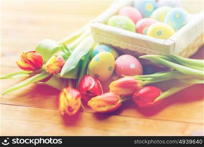 Easter, holidays, tradition and object concept - close up of colored easter eggs in basket and tulip flowers. close up of colored easter eggs and flowers