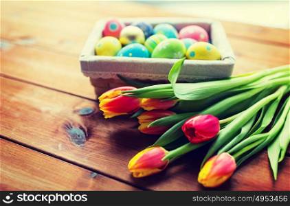 easter, holidays, tradition and object concept - close up of colored easter eggs in basket and tulip flowers. close up of colored easter eggs and flowers